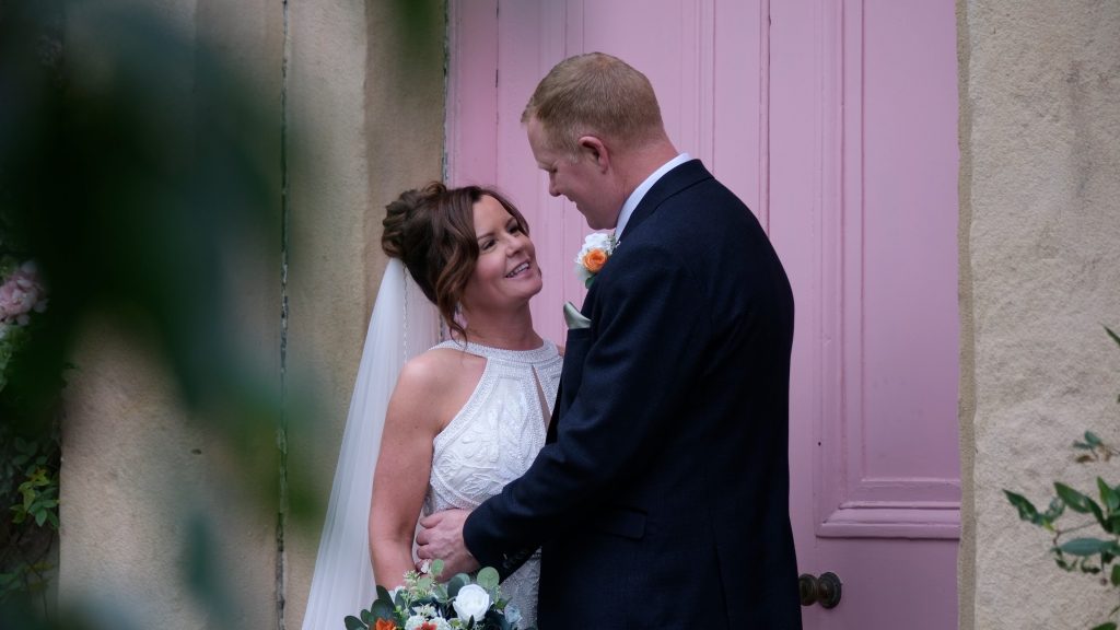 Bride and groom standing together in front of the pink door at The Croft Hotel, dressed in wedding attire. Wedding Video at The Croft.