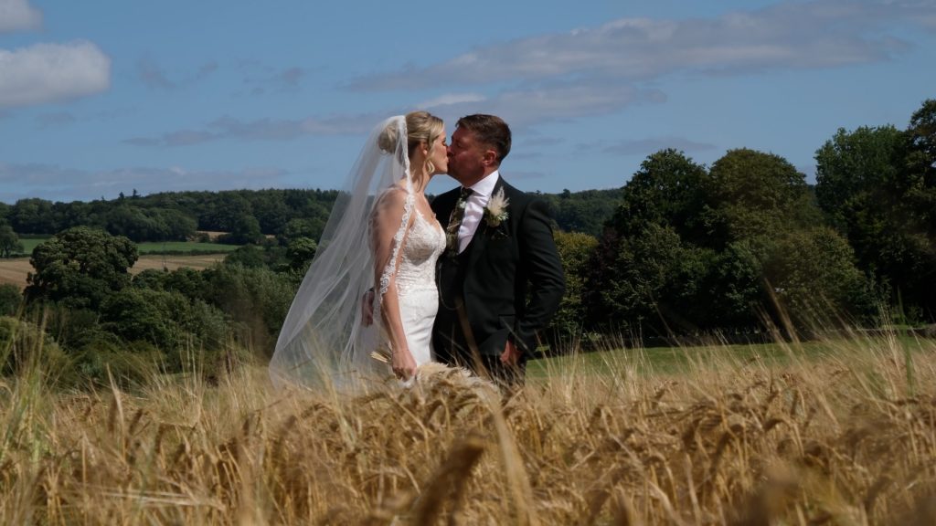 Bride and groom standing side by side in a golden cornfield at the Yorkshire Wedding Barn on their wedding day, smiling and holding hands amid the rural countryside. Yorkshire Wedding Barn Wedding Film